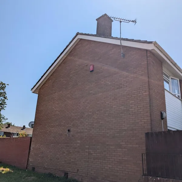 Brick gable end wall and chimney stack with TV aerial under a blue sky