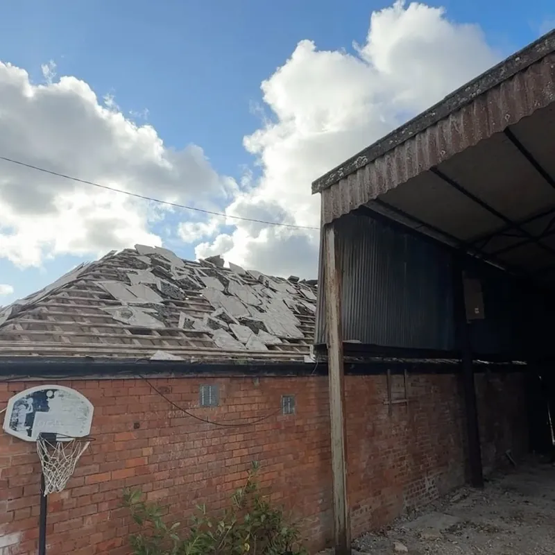 Roof with broken and missing tiles after a storm, beside a brick garage